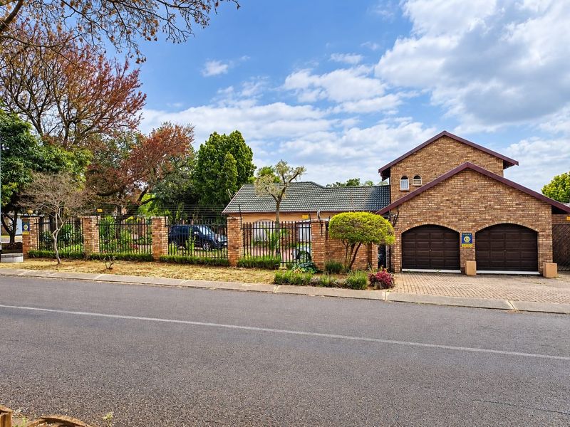 Front view of a face brick house featuring a double garage, paved driveway, and secure perimeter fencing with electric security wires.