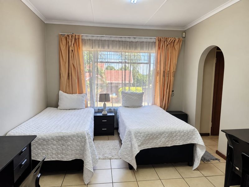 A functional bedroom featuring tiled flooring, an arched entryway, and a large window with security bars, providing natural light.