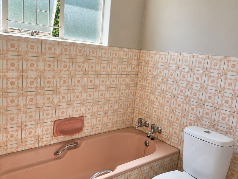 A functional bathroom featuring a vintage pink bathtub, matching wall tiles, and a standard white toilet, offering potential for a modern renovation.