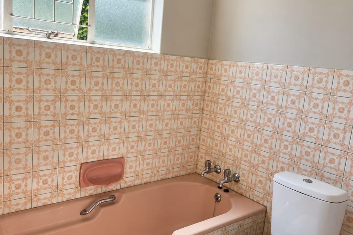A functional bathroom featuring a vintage pink bathtub, matching wall tiles, and a standard white toilet, offering potential for a modern renovation.