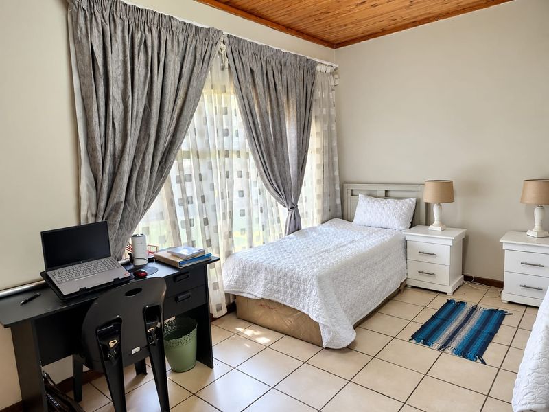A bedroom featuring tiled flooring and a timber ceiling, providing a functional space with natural light through large windows.