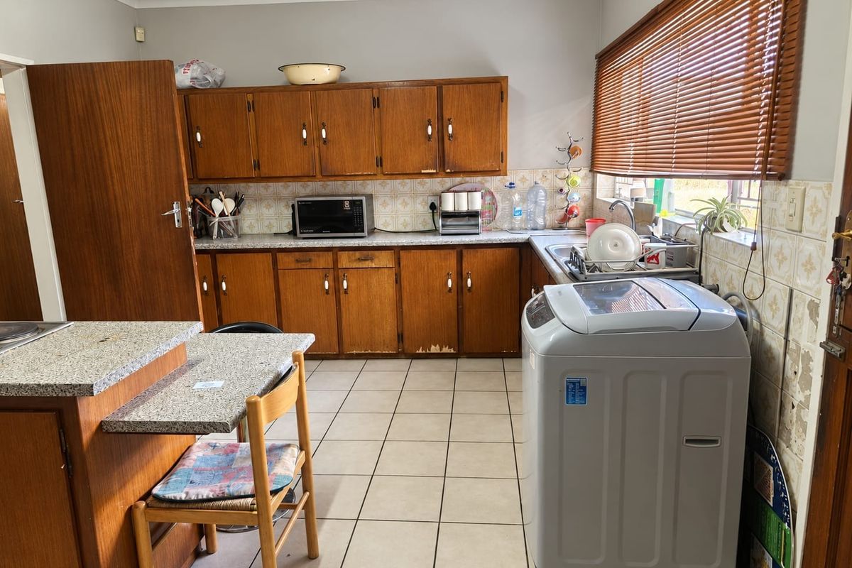A functional kitchen featuring wooden cabinetry, granite-look countertops, and ceramic tile flooring, offering a practical layout with potential for modern updates.