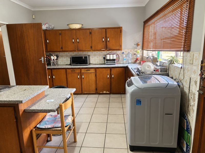 A functional kitchen featuring wooden cabinetry, granite-look countertops, and ceramic tile flooring, offering a practical layout with potential for modern updates.