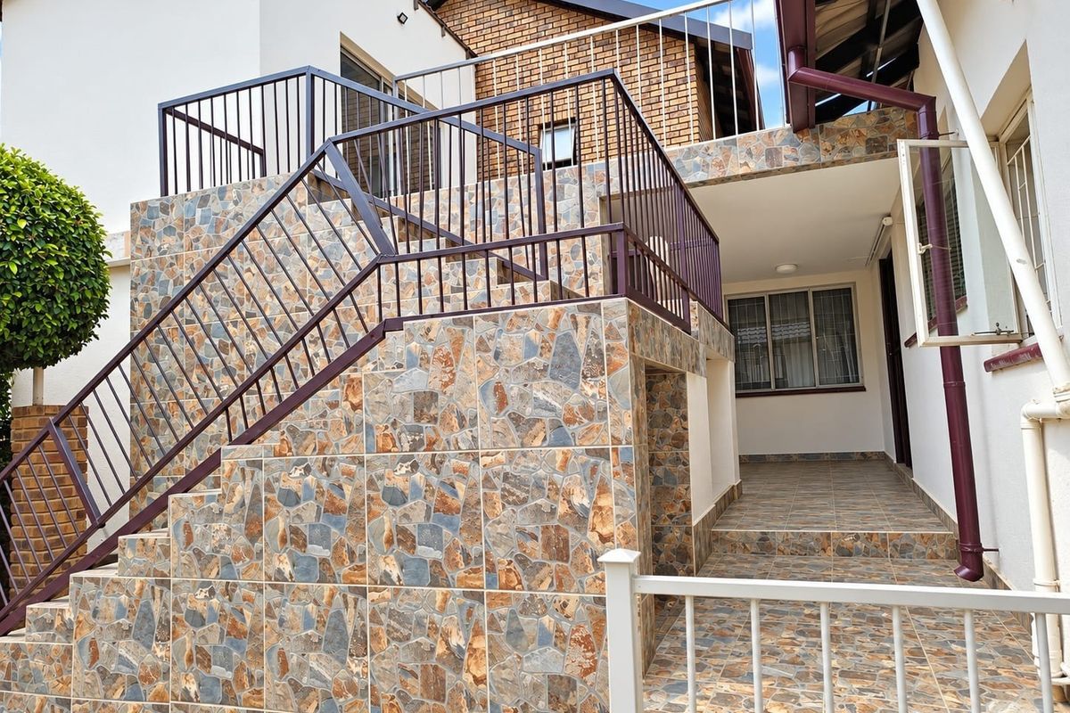 Rear exterior view featuring a stone-clad staircase with metal railings leading to an upper level, complemented by a tiled patio area.