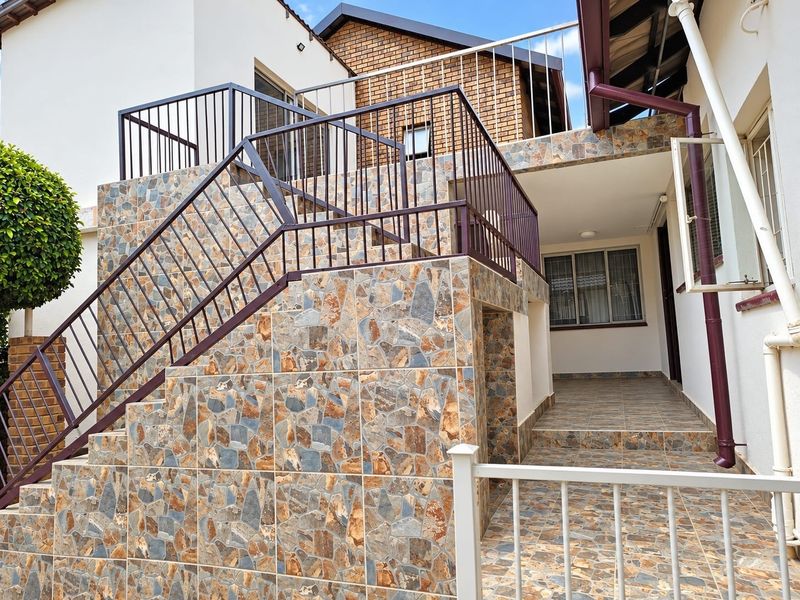 Rear exterior view featuring a stone-clad staircase with metal railings leading to an upper level, complemented by a tiled patio area.