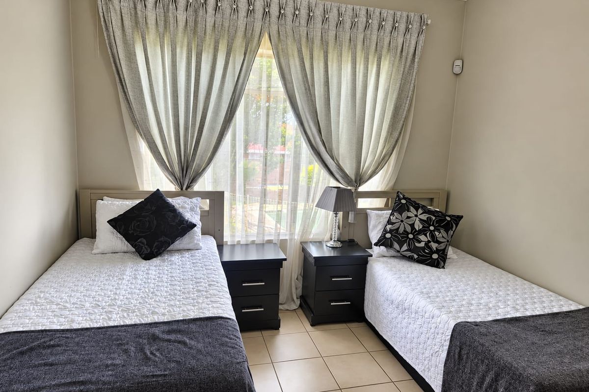 A functional bedroom featuring tiled flooring and a window with installed curtain tracks, providing a neutral space ready for personalization.