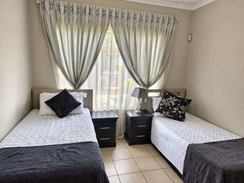A functional bedroom featuring tiled flooring and a window with installed curtain tracks, providing a neutral space ready for personalization.