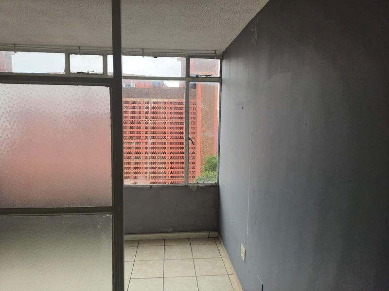 An enclosed balcony or sunroom featuring tiled flooring, aluminium-framed windows with textured glass, and grey painted walls.