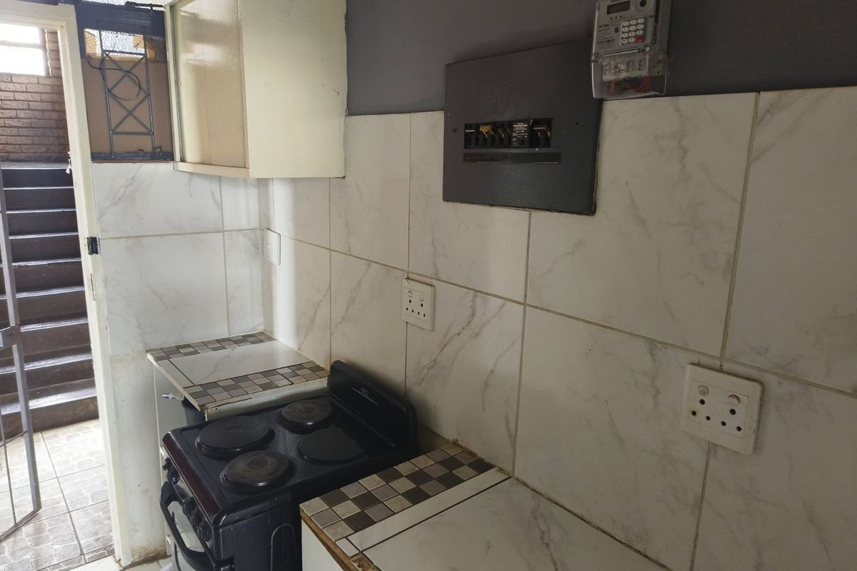 A compact kitchen area featuring a built-in electric stove, tiled backsplash, and wall-mounted cabinetry, with an integrated prepaid electricity meter and distribution board.