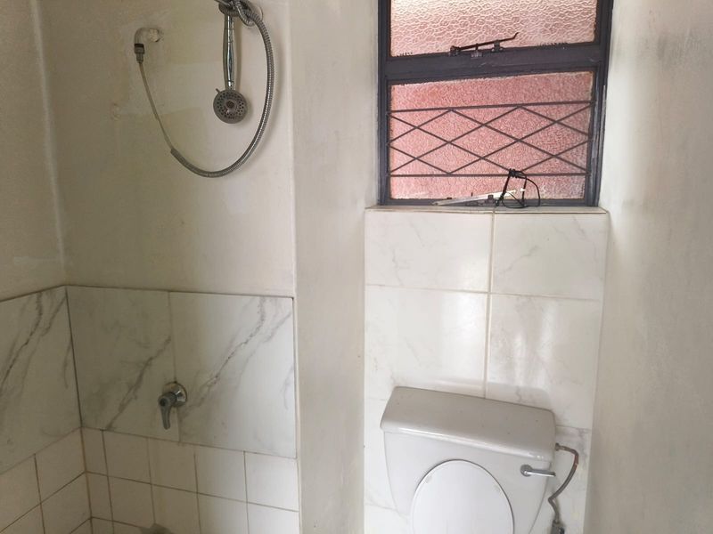 A compact bathroom featuring a shower and toilet, requiring renovation to update the dated finishes and address wall surface damage.