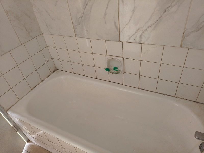 A bathroom featuring a standard bathtub with white wall tiling and a built-in recessed soap dish.