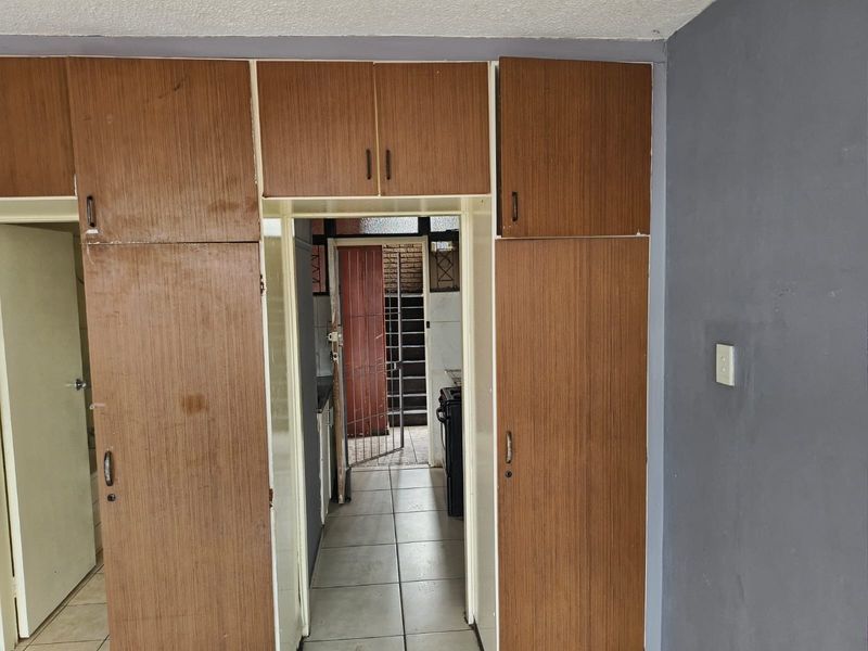 A hallway featuring built-in wooden cupboards and tiled flooring, providing access to adjacent rooms and a rear entrance with a security gate.