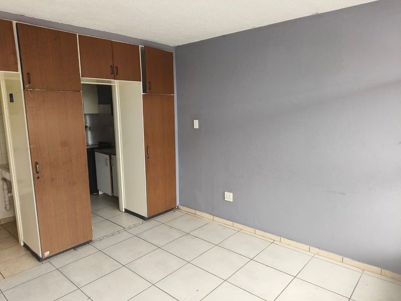 An empty bedroom featuring tiled flooring and built-in wooden cupboards, offering a blank canvas for renovation or interior design updates.