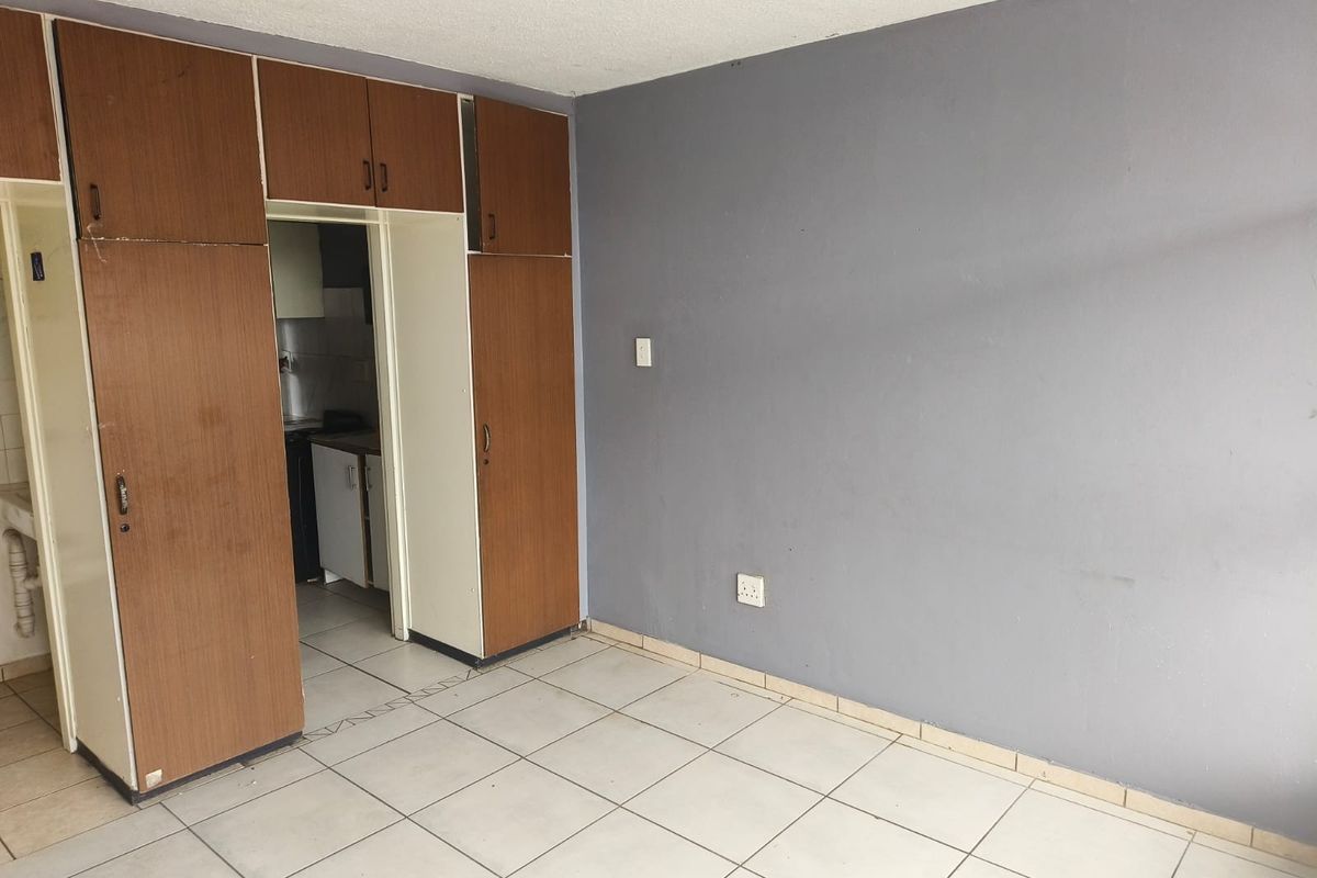 An empty bedroom featuring tiled flooring and built-in wooden cupboards, offering a blank canvas for renovation or interior design updates.