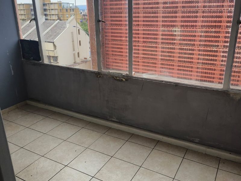 An enclosed balcony area featuring tiled flooring and large windows with urban views, requiring maintenance and cosmetic updates.