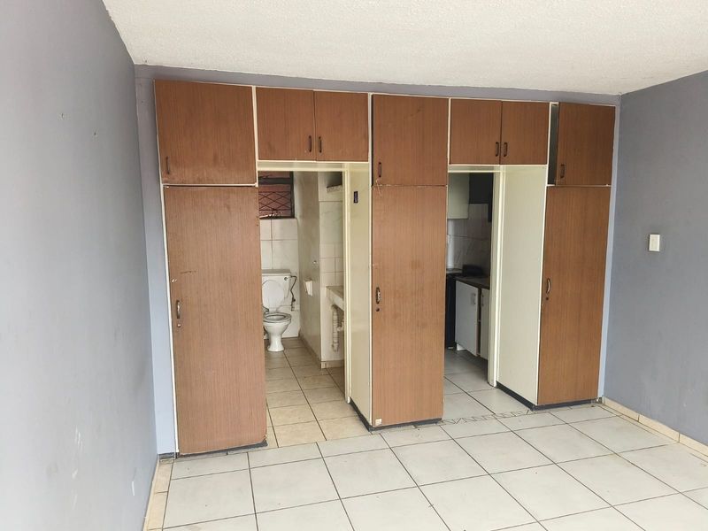 Open plan living area featuring built-in cupboards with direct access to a small bathroom and kitchen area.