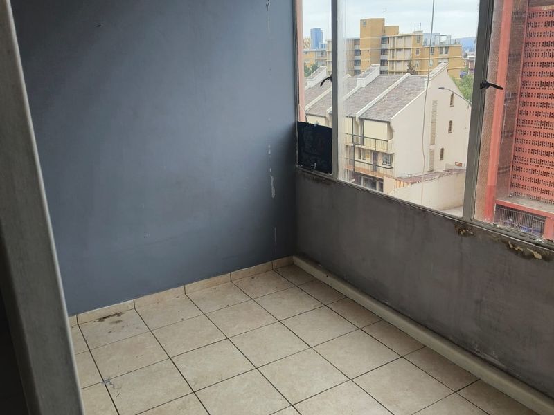An enclosed balcony space featuring tiled flooring and large windows with urban views, currently requiring cosmetic refurbishment and wall repairs.