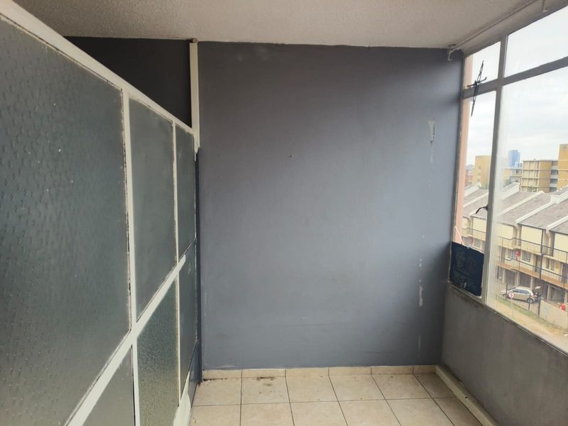 An enclosed balcony area featuring tiled flooring, large aluminium-framed windows, and a frosted glass partition, offering a versatile space for potential use.