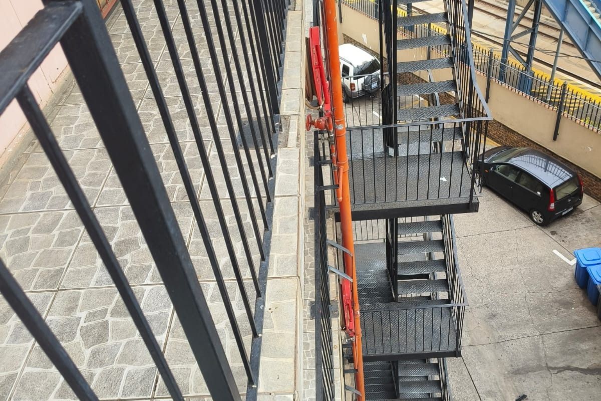 An elevated view of a stone-tiled balcony featuring a black metal balustrade and an external metal fire escape staircase.