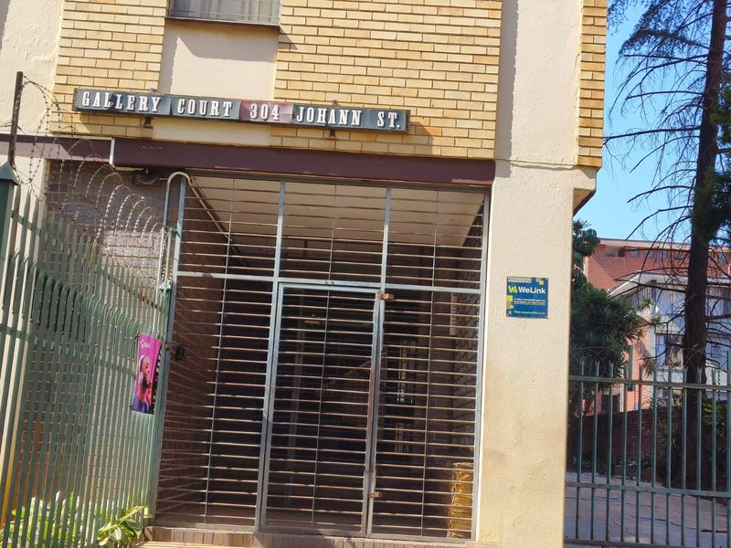 Front entrance of Gallery Court apartment building featuring brick facade, security gate, and perimeter metal fencing.