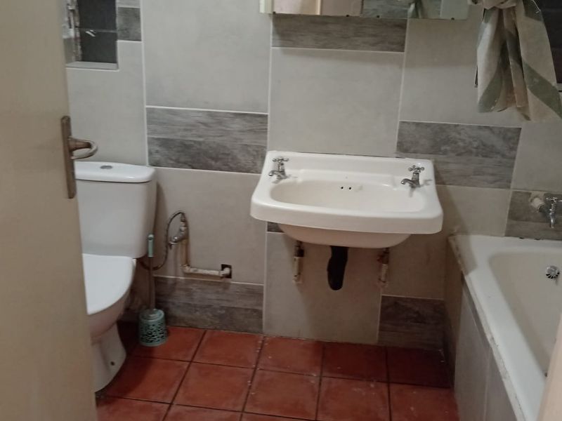 A functional bathroom featuring a wall-mounted basin, toilet, and bathtub with tiled finishes throughout.
