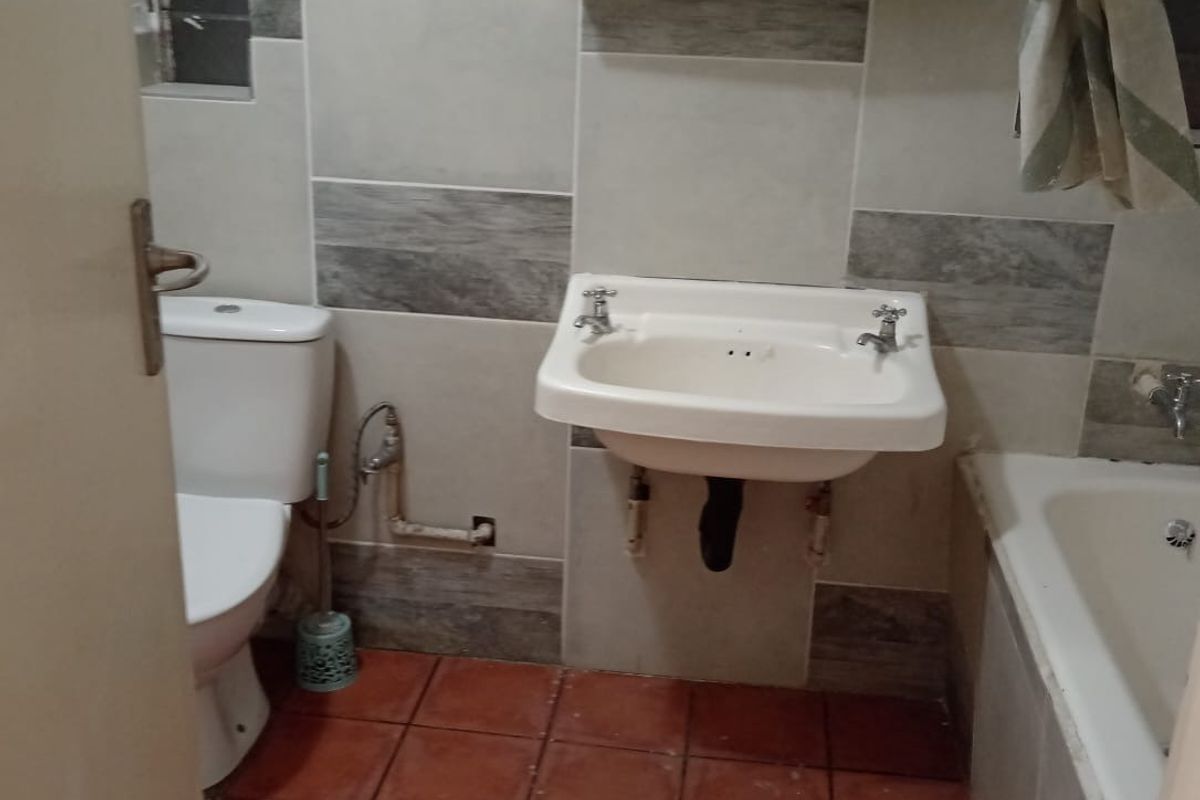 A functional bathroom featuring a wall-mounted basin, toilet, and bathtub with tiled finishes throughout.