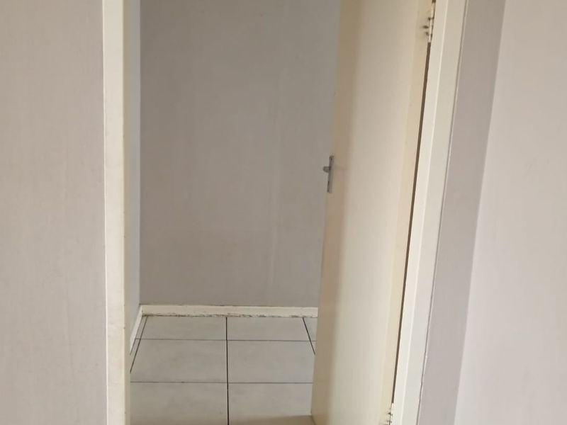 A vacant hallway featuring neutral wall paint and tiled flooring, providing access to an adjacent room through a standard internal door.