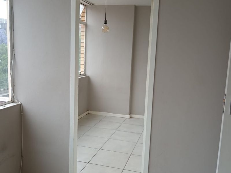 An empty, neutral-toned hallway featuring tiled flooring and a simple pendant light fixture, connecting two interior spaces.
