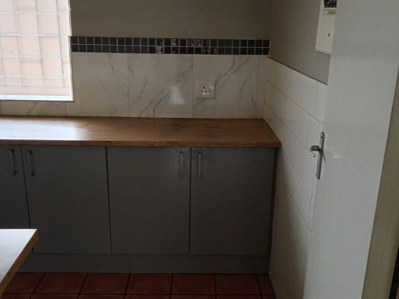 A functional kitchen area featuring grey built-in cabinetry, a wooden countertop, tiled splashback, and ceramic floor tiles, providing a practical workspace.