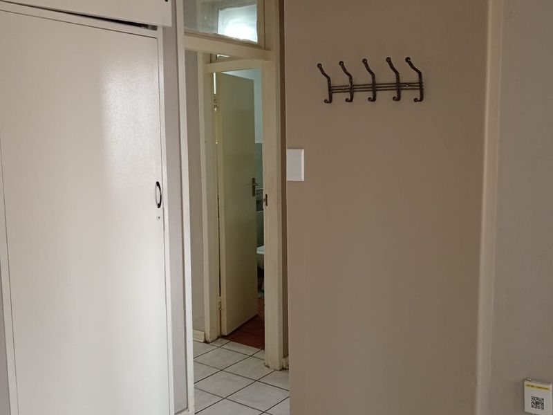 A functional hallway featuring tiled flooring, a built-in storage cupboard, and a transom window leading to an adjacent room.