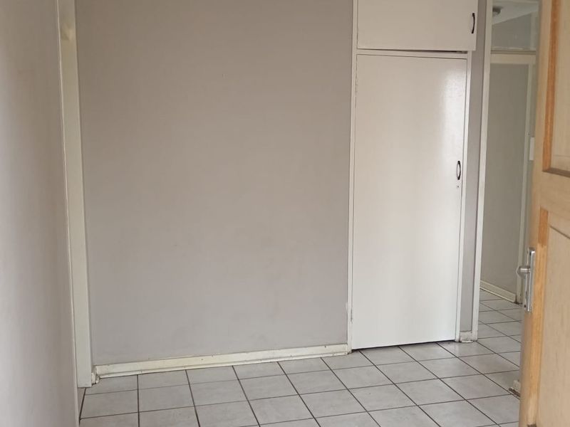 An empty bedroom featuring tiled flooring and a built-in cupboard with overhead storage.