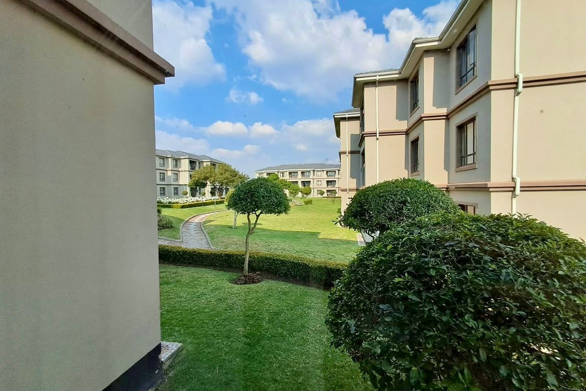 A view of the well-maintained communal garden and landscaped grounds between apartment blocks, featuring paved pathways and manicured hedges.