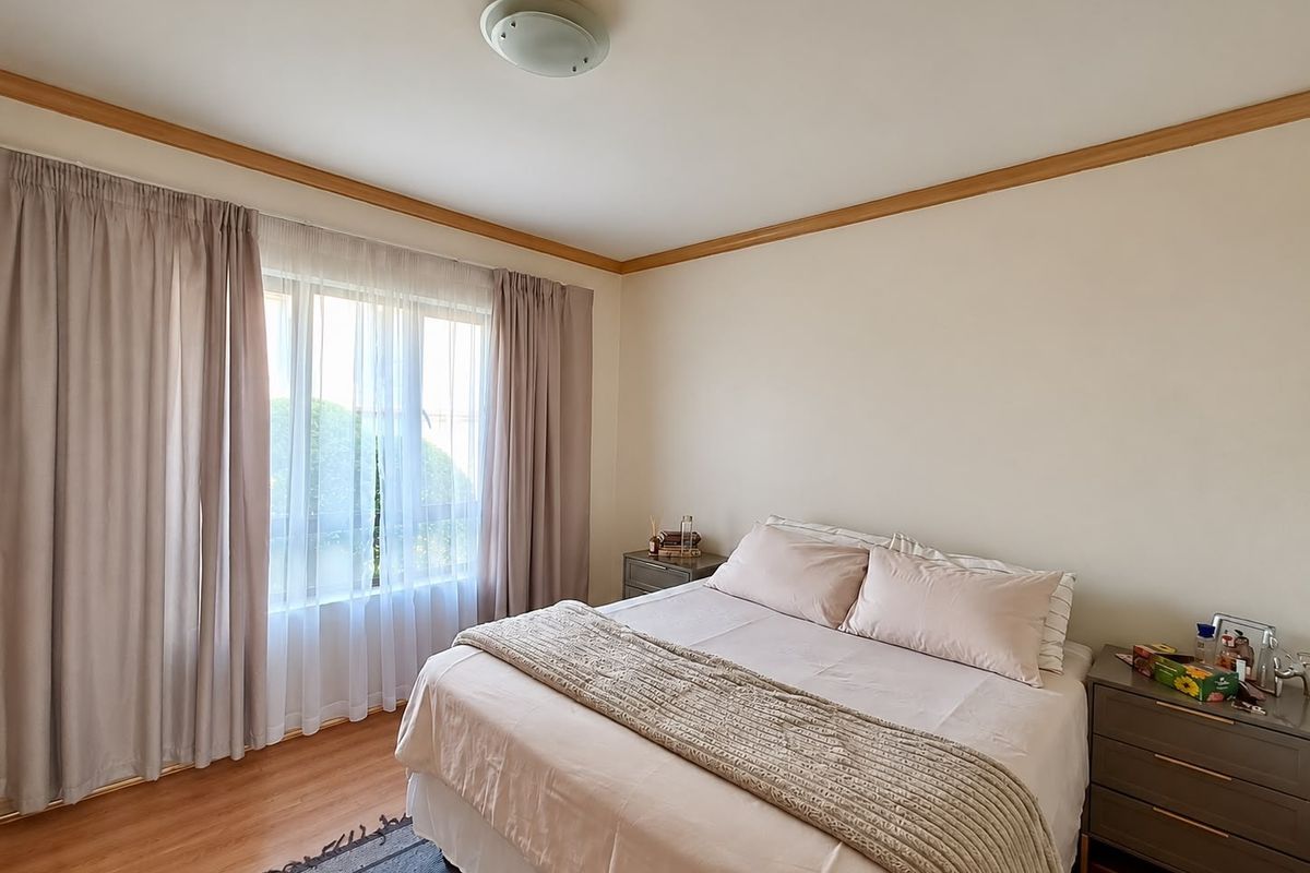 A well-maintained bedroom featuring laminate flooring, timber crown molding, and a large window with natural light.