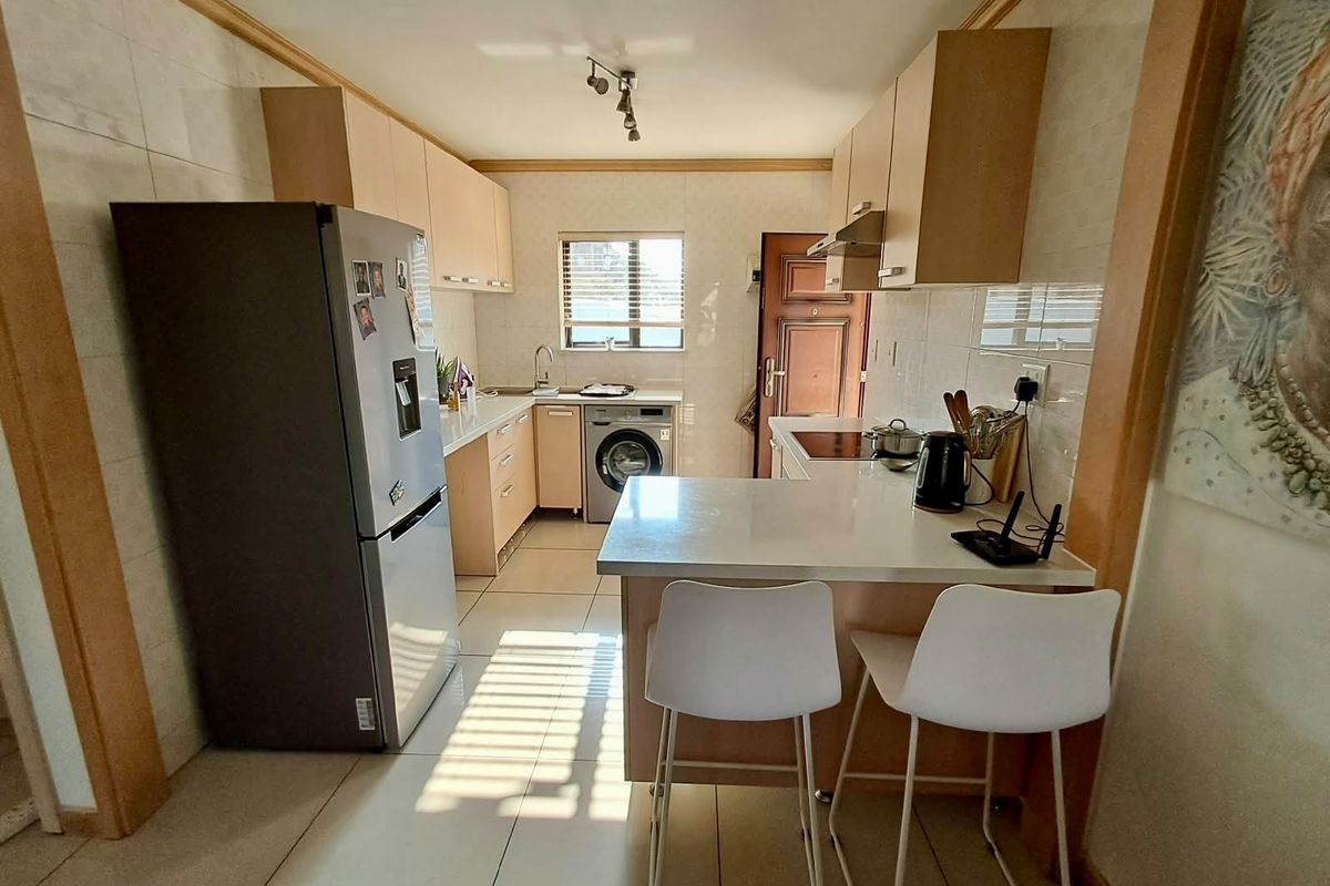 A functional kitchen featuring light wood cabinetry, stone countertops, a breakfast bar, and integrated appliances, with tiled flooring and backsplash throughout.