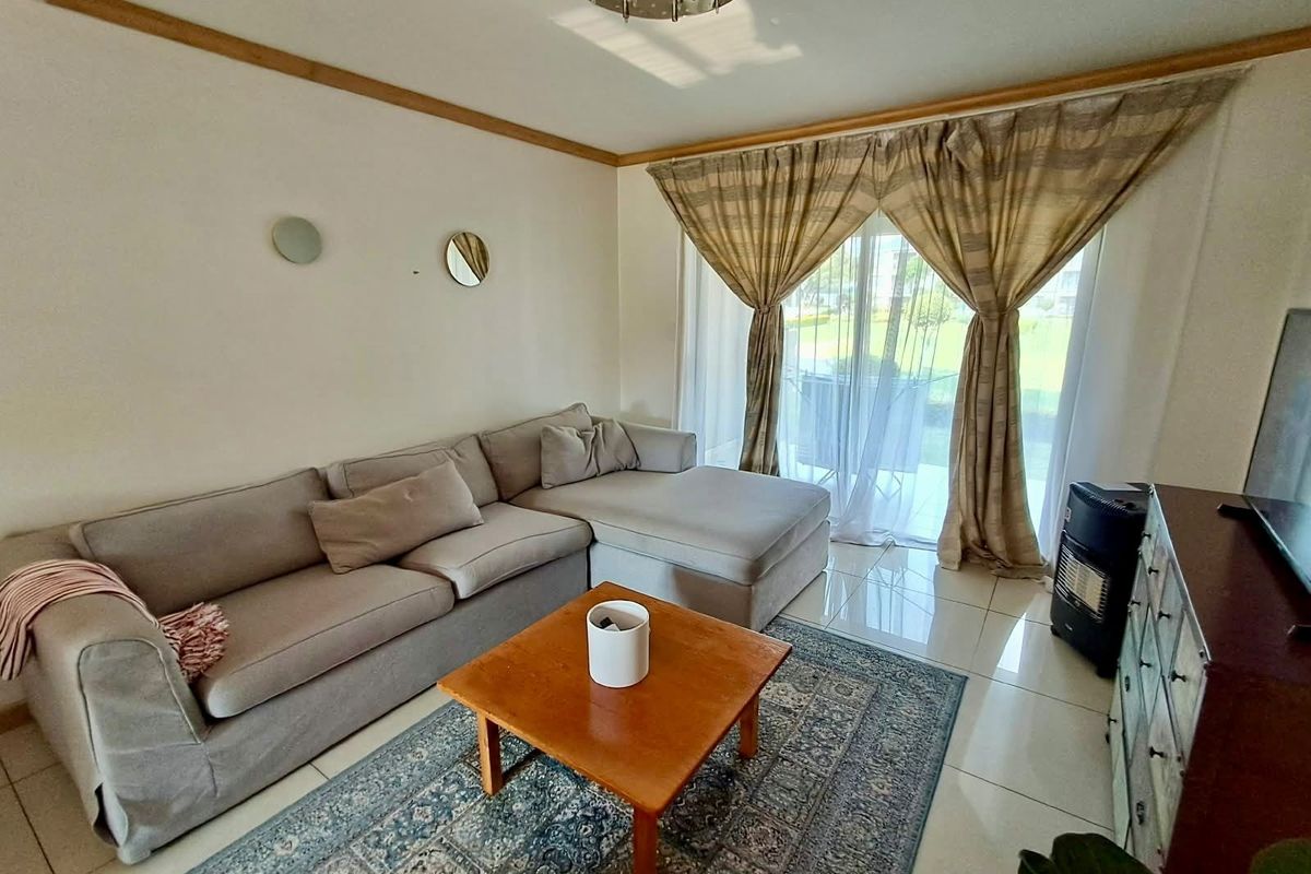 A bright living room featuring tiled flooring, crown molding, and a sliding glass door providing access to the outdoor area.