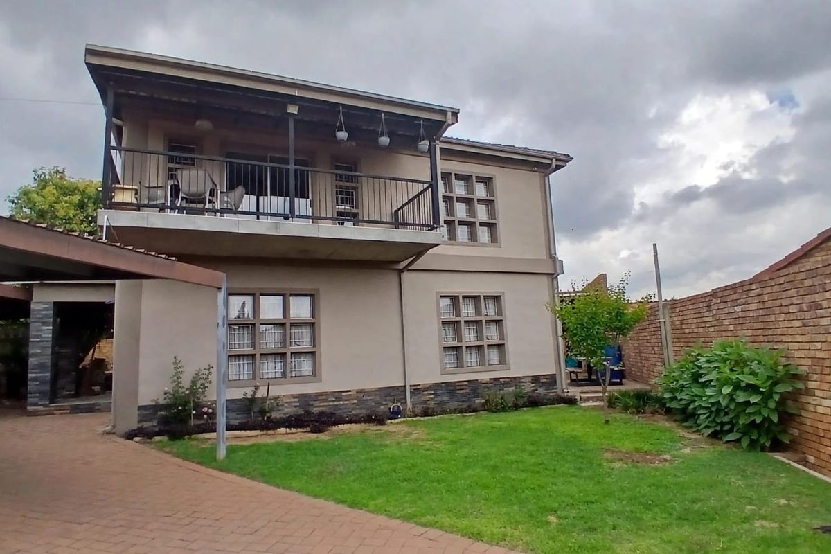 Rear view of a two-story house featuring a balcony, stone cladding accents, a paved driveway, and a brick boundary wall.
