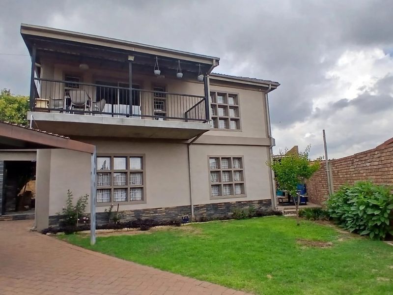 Rear view of a two-story house featuring a balcony, stone cladding accents, a paved driveway, and a brick boundary wall.