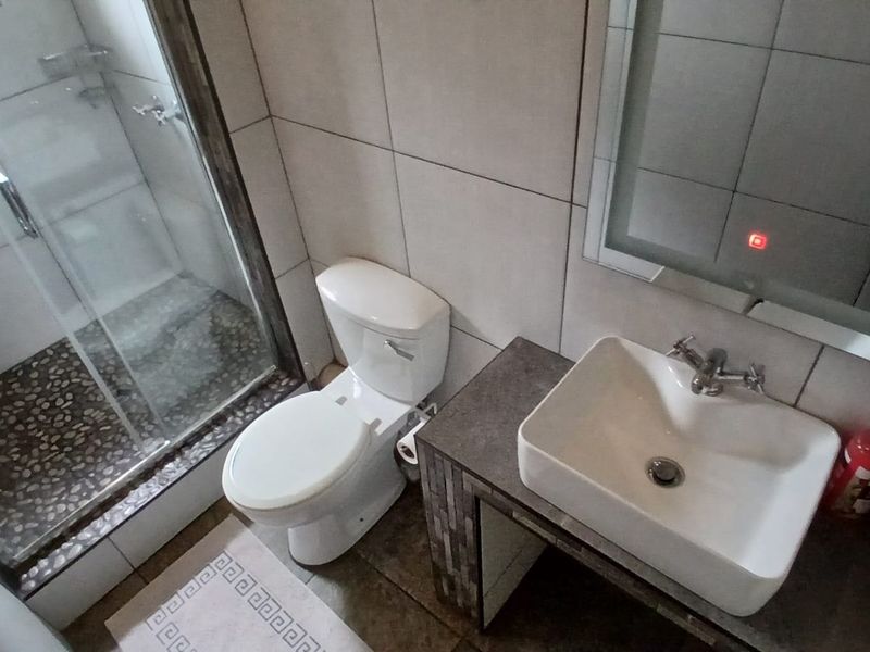 Modern bathroom featuring a glass-enclosed shower with pebble flooring, a vessel sink vanity, and a contemporary lighted mirror.