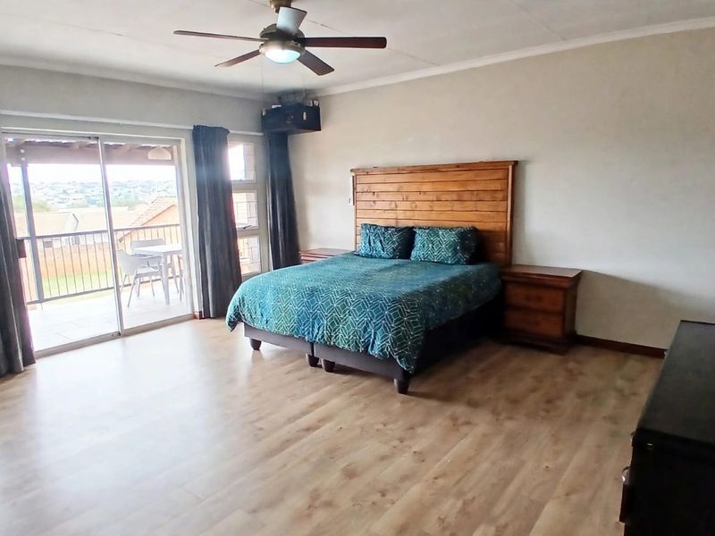 Spacious bedroom featuring laminate flooring, a ceiling fan, and large sliding glass doors that open onto a private balcony.