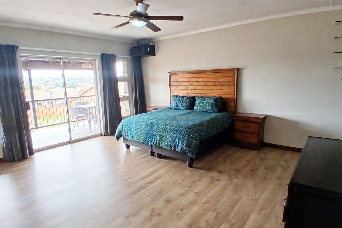 Spacious bedroom featuring laminate flooring, a ceiling fan, and large sliding glass doors that open onto a private balcony.