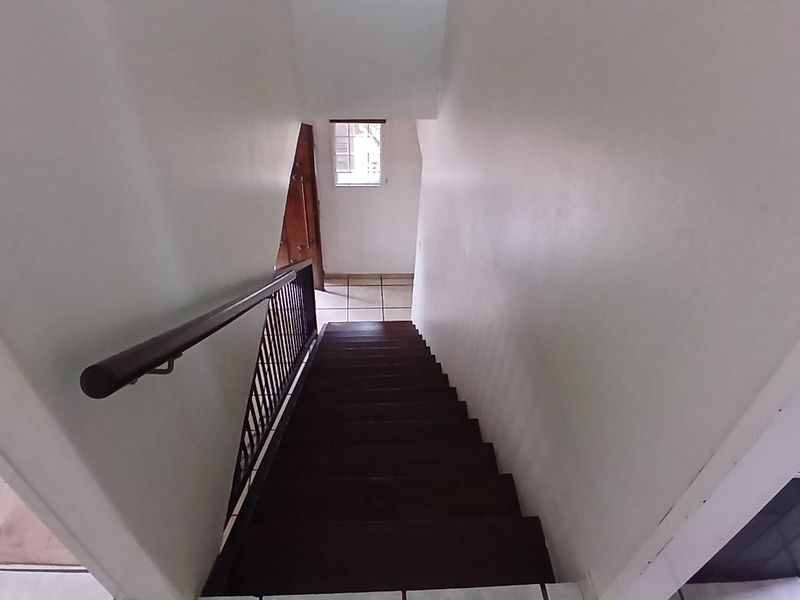 A staircase with dark wooden treads, a metal balustrade, and a wooden handrail leading down to a tiled landing area.