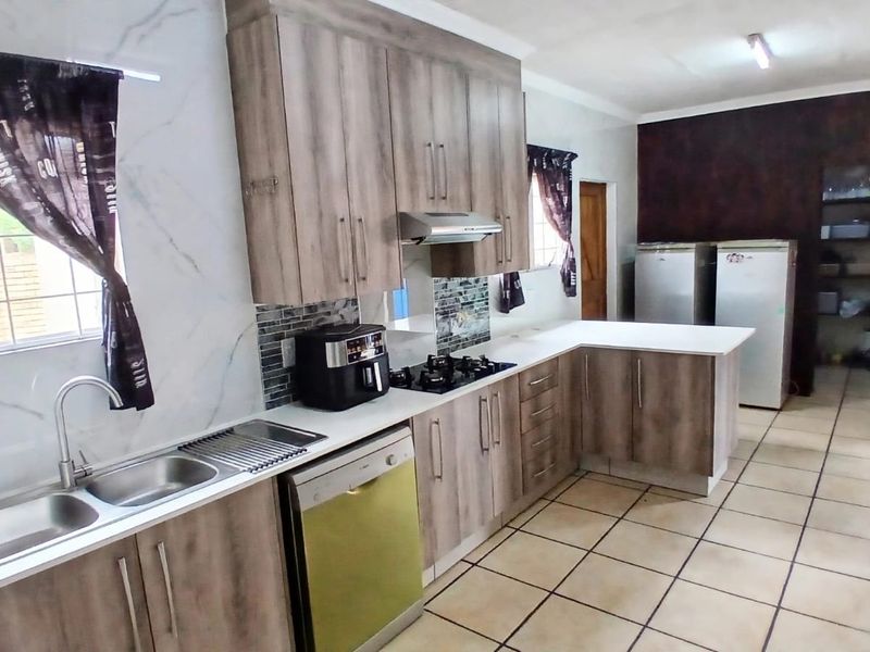 A functional kitchen featuring wood-look cabinetry, gas hob, extractor fan, double sink, and tiled flooring with a neutral aesthetic.