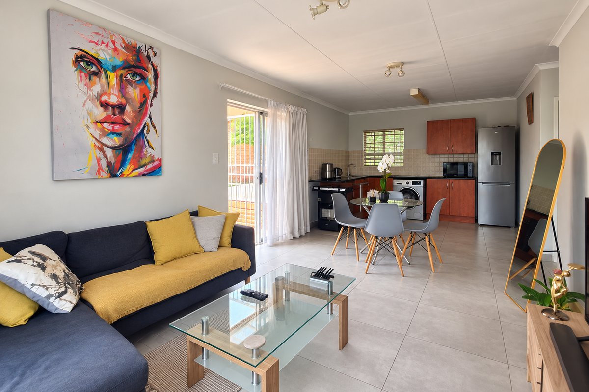 A bright open-plan living and kitchen area featuring neutral tiled flooring, modern cabinetry, and direct access to an outdoor patio through sliding glass doors.