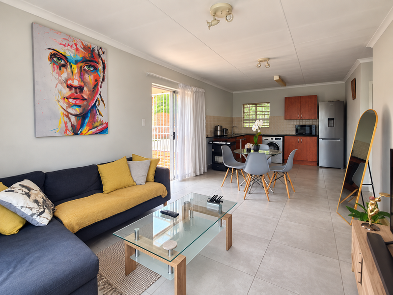 A bright open-plan living and kitchen area featuring neutral tiled flooring, modern cabinetry, and direct access to an outdoor patio through sliding glass doors.
