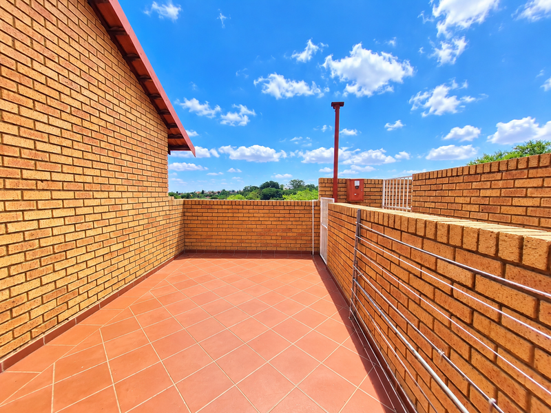 An open-air balcony featuring brick walls and tiled flooring, offering a clear view of the surrounding area.