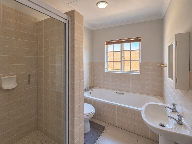A clean, functional bathroom featuring a separate shower enclosure, bathtub, pedestal basin, and toilet with neutral wall and floor tiling.