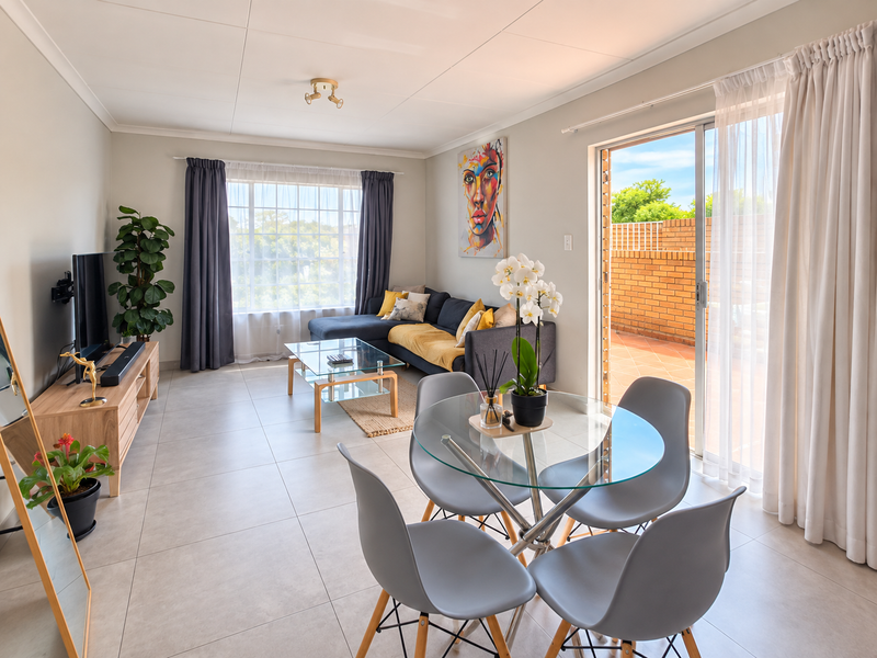 Bright open-plan living and dining area featuring neutral tiled flooring, modern cove cornicing, and a large sliding glass door leading to an outdoor patio.