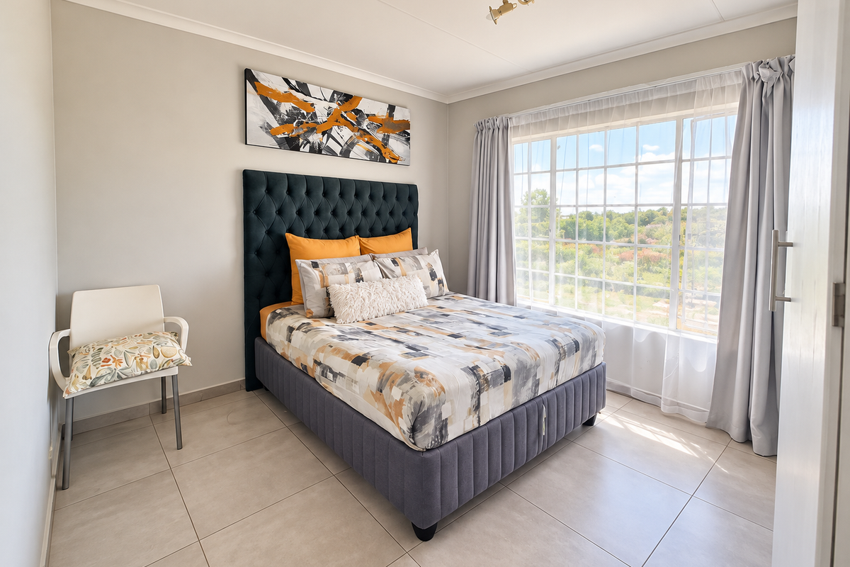 A bright and well-maintained bedroom featuring neutral tiled flooring, a large window with natural light, and a clean, modern aesthetic.