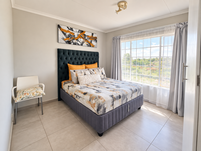 A bright and well-maintained bedroom featuring neutral tiled flooring, a large window with natural light, and a clean, modern aesthetic.