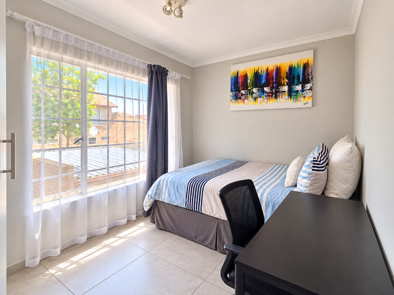 A bright and well-maintained bedroom featuring large windows, neutral wall finishes, and tiled flooring, offering a comfortable and functional living space.